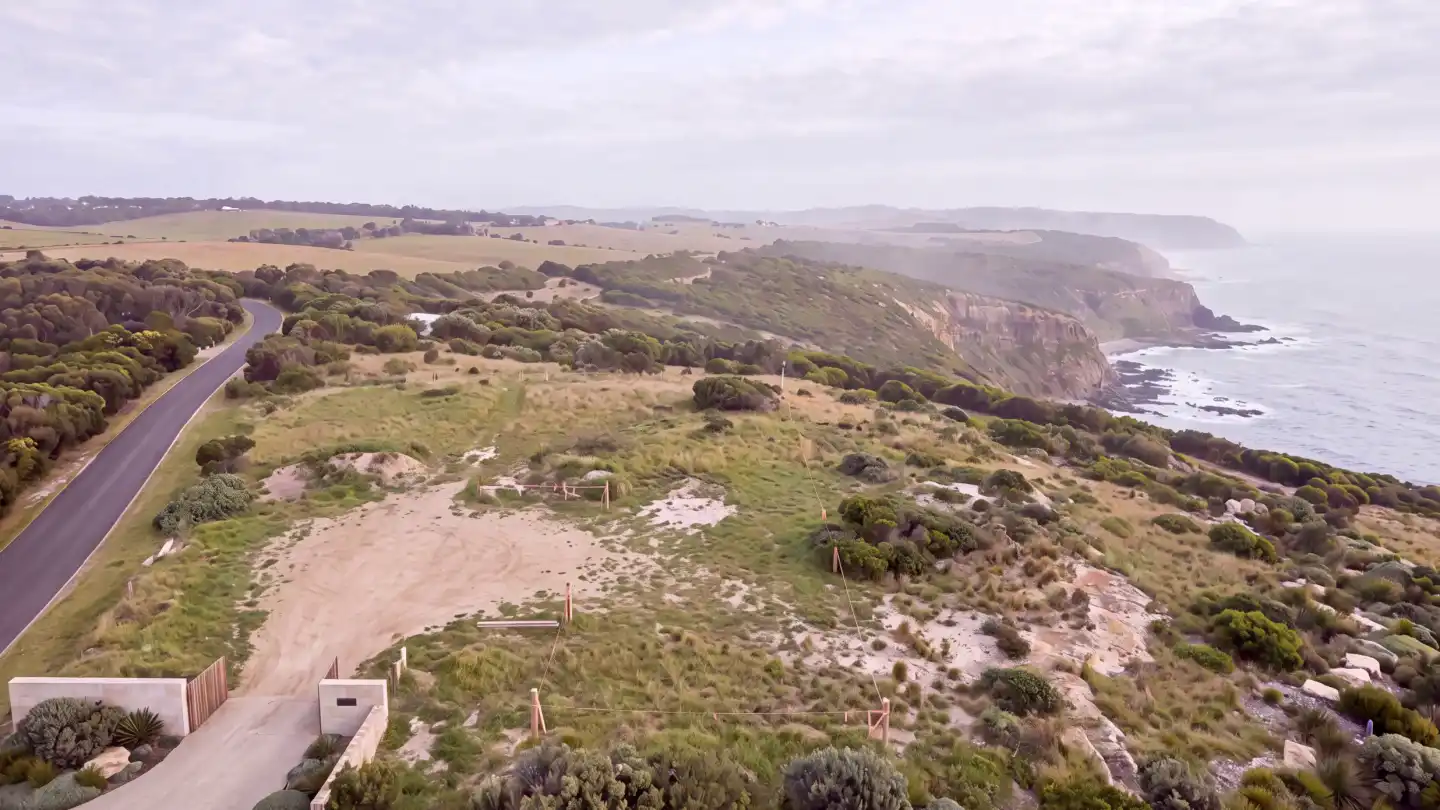 The bare clifftop site: excavated platform, fresh slab, a tower crane against the ocean.